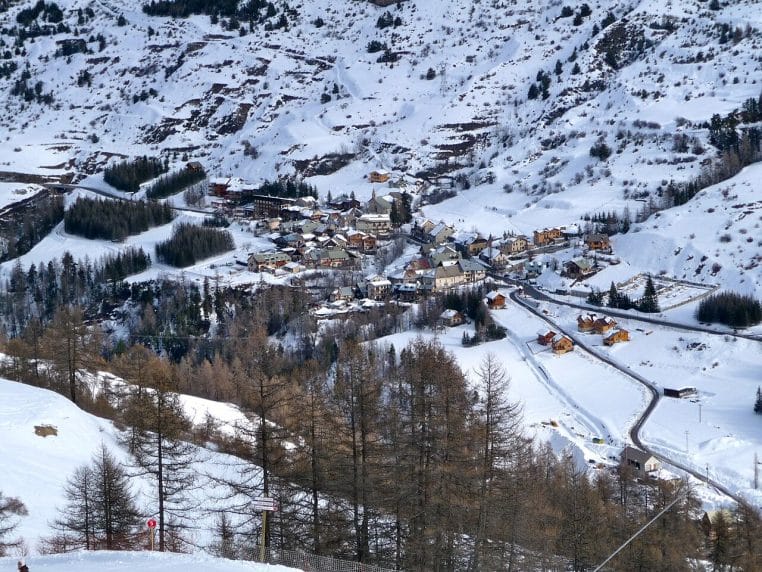 Vue en hauteur sur le village de Vars Saint-Marcelin entouré de pentes enneigées, de chalets et de forêts de conifères en hiver.