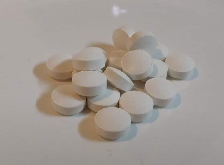 Petit tas de comprimés blancs de vitamine D posés sur une assiette claire, évoquant une supplémentation encadrée médicalement