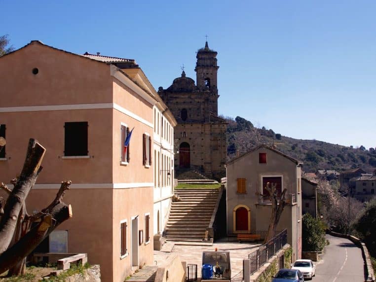 Façade ocre de la mairie-école communale de Volpajola, avec escalier monumental menant à l’église au cœur du village corse.
