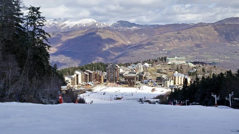Front de neige d’Ax 3 Domaines vu depuis la piste Bonascre, bâtiments et télésièges sous une couche fraîche en fin d’hiver.