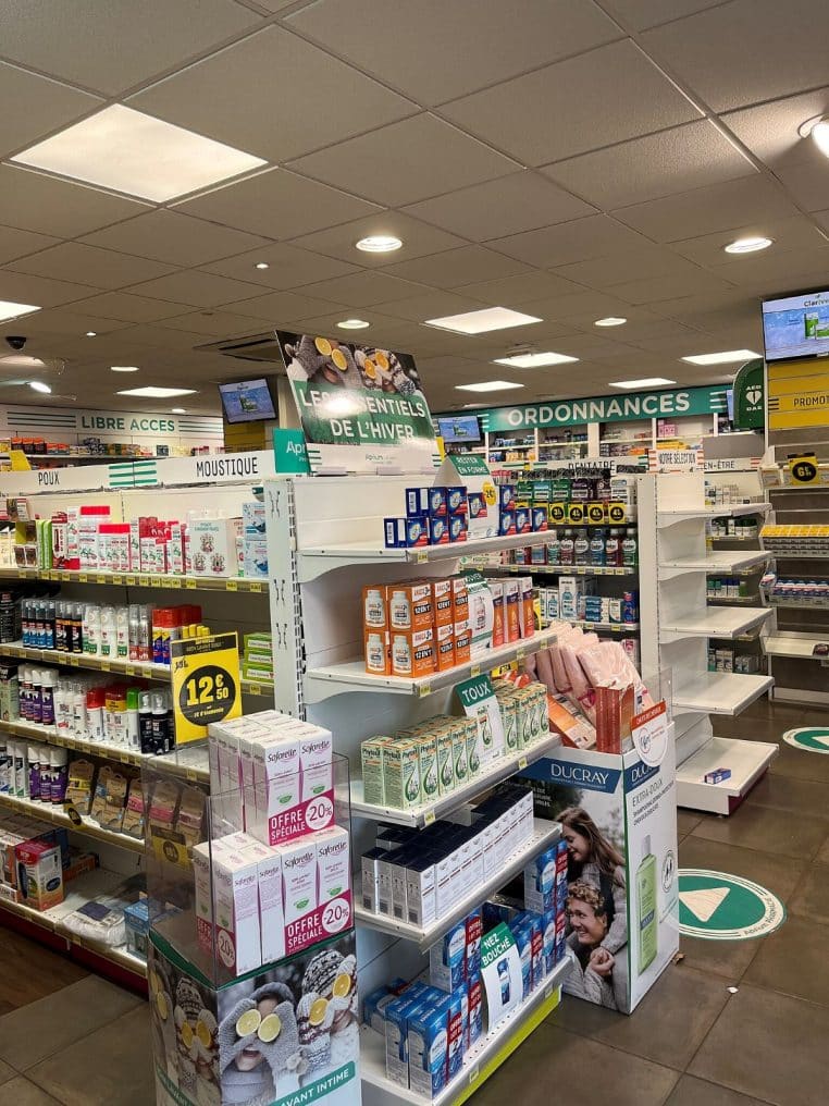 Vue intérieure d’une pharmacie moderne en France avec allées de produits et signalétique santé bien-être.