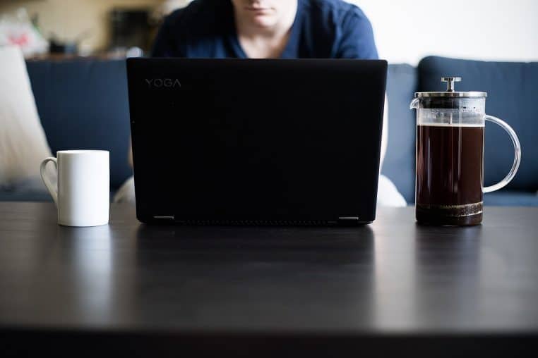 Ordinateur portable sur table basse, tasse et cafetière à proximité : un poste de télétravail improvisé dans le salon d’un logement.