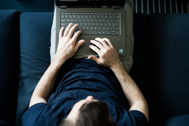 Vue au-dessus d’une personne travaillant sur un ordinateur portable depuis un canapé, posture décontractée en environnement domestique.
