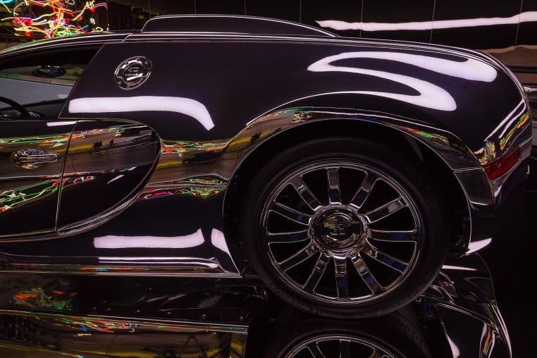 Vue rapprochée de l’aile arrière et de la roue d’une Bugatti Veyron noire très brillante, reflétant les lumières d’un showroom automobile.
