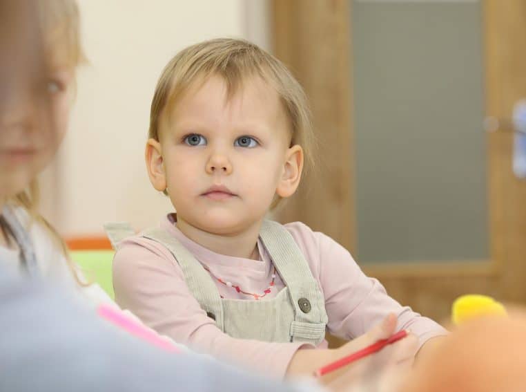 Groupe d’enfants assis en classe de maternelle, concentrés autour d’une table, avec une adulte qui les accompagne dans une activité éducative.