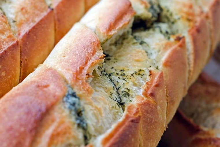 Gros plan sur une baguette dorée coupée en tranches, garnie de beurre aux herbes, mettant en valeur sa croûte croustillante.