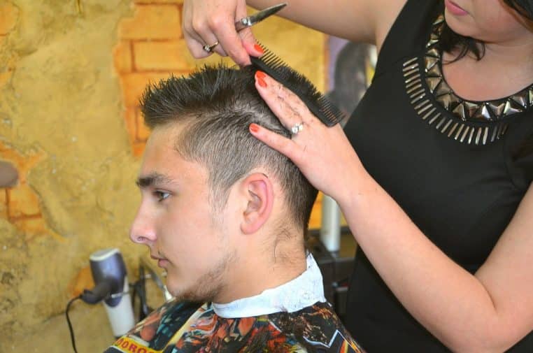 Coiffeuse coupant les cheveux courts d’un jeune homme assis au bac dans un salon, concentrée sur la forme de la coupe
