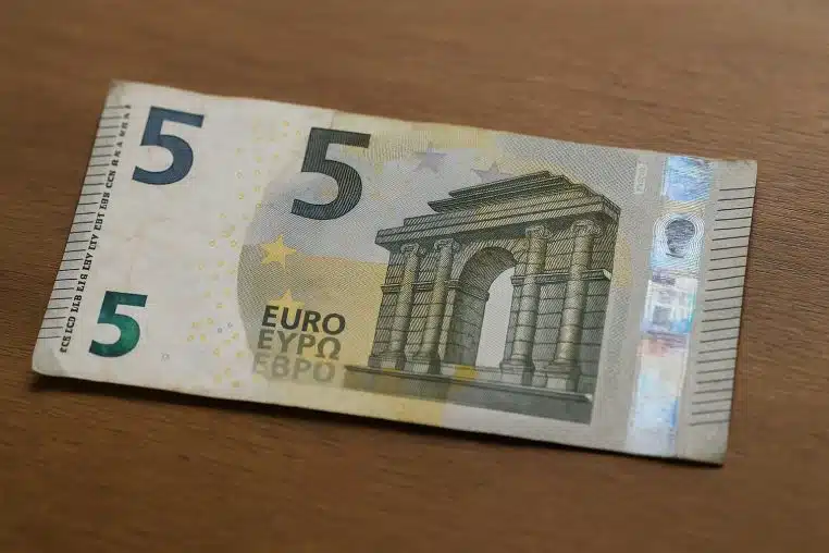 Billet de 5 euros légèrement usé posé à plat sur une table en bois, montrant clairement l’arc et les détails de sécurité.
