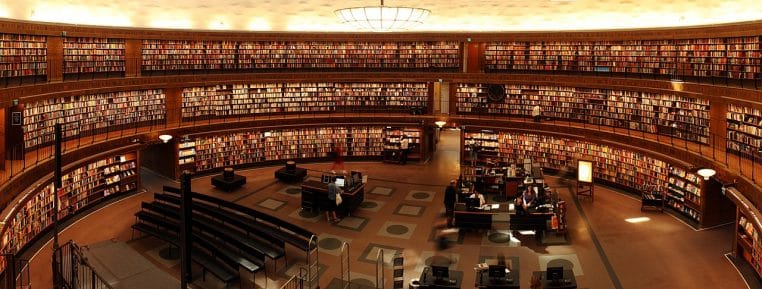 Immense bibliothèque circulaire avec rayonnages sur plusieurs étages et lecteurs installés aux tables de travail au centre de la salle