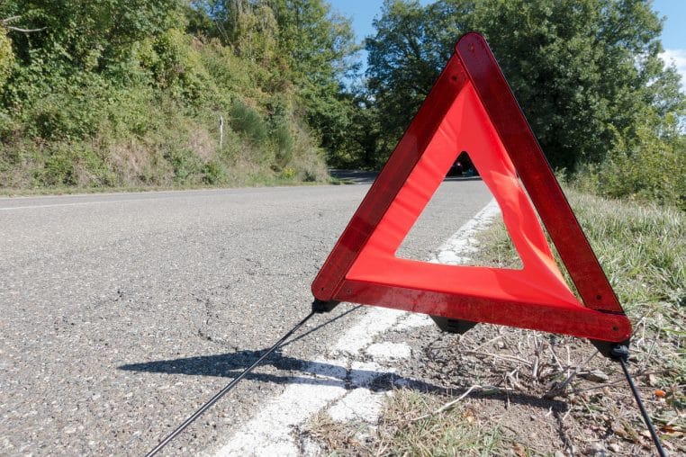 Triangle de présignalisation rouge installé au ras de la chaussée sur une route de campagne, pour signaler un véhicule en panne hors champ