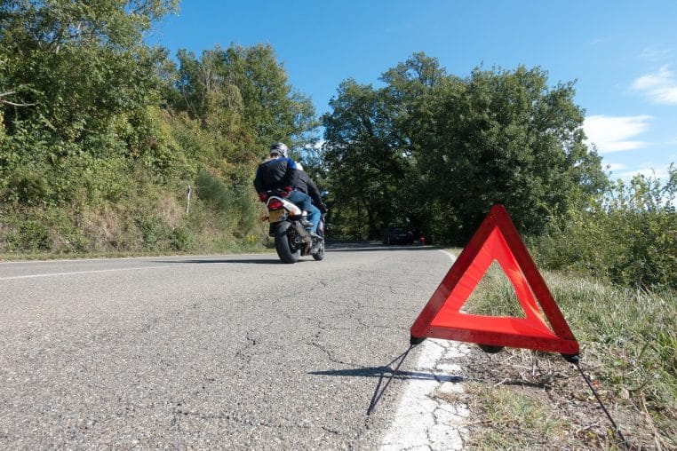 Triangle de présignalisation posé sur la chaussée devant une voiture immobilisée signalant un arrêt d’urgence sur route.