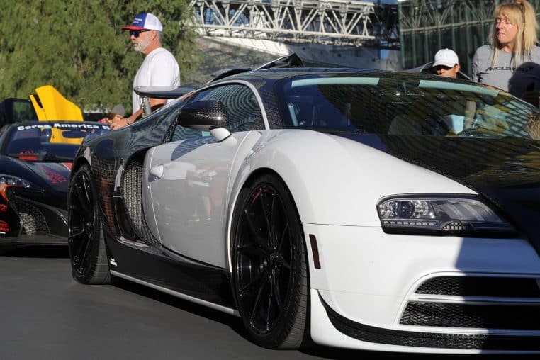 Bugatti Veyron blanche et noire garée en extérieur lors d’un rassemblement, entourée de passionnés observant la supercar de près.