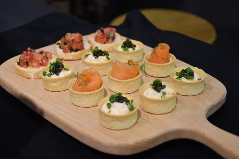 Planche en bois garnie de petits canapés au saumon et œufs de poisson, parfaite pour un apéritif festif et élégant.
