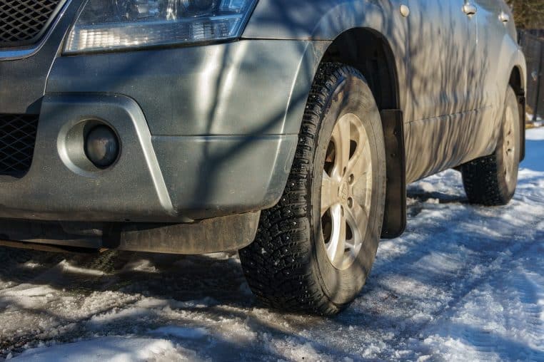 Voiture roulant sur une route de campagne enneigée, pneus hiver au premier plan projetant la neige fondante sur l’asphalte.