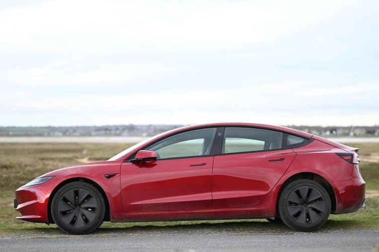 Profil d’une Tesla rouge garée en rase campagne, utilisée pour illustrer l’usure des trains roulants des véhicules électriques modernes