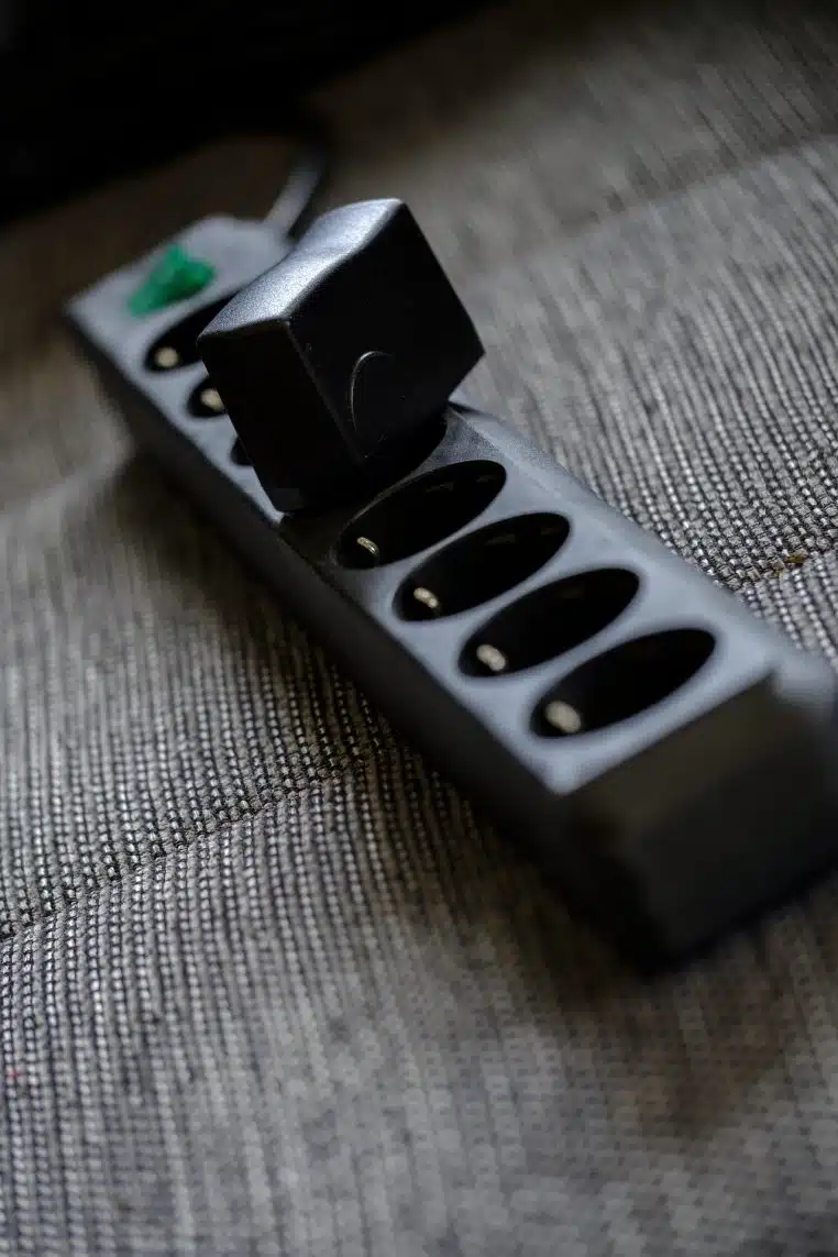 Gros plan sur une multiprise chargée de chargeurs et de blocs secteurs branchés ensemble sur un sol clair, symbole de la consommation fantôme au quotidien.