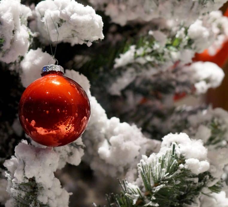 Sapin de Noël enneigé en gros plan avec boules rouges et décorations scintillantes sur un fond de vitrine floue
