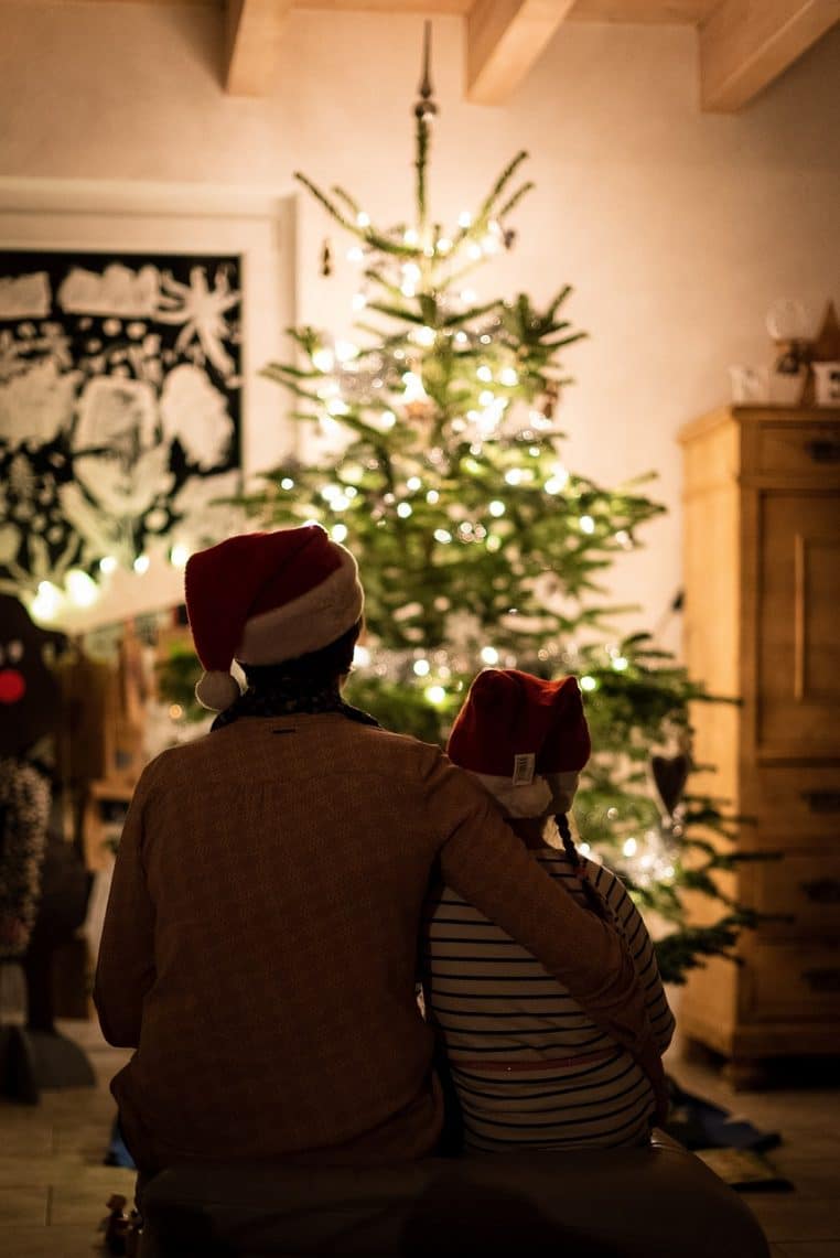 Famille réunie devant le sapin ouvrant des cadeaux de Noël, ambiance chaleureuse de salon éclairé aux décorations de fête