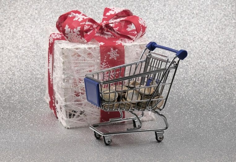 Personne tenant une carte bancaire et des paquets cadeaux rouges, décor de Noël flou en arrière-plan dans une rue commerçante