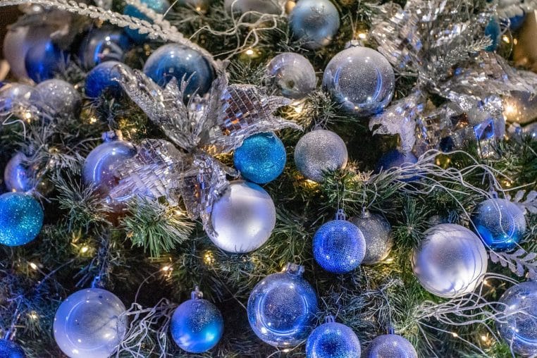 Sapin de Noël artificiel enneigé, décoré de guirlandes et boules dorées dans un intérieur contemporain