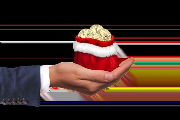 Main tendant un billet d’argent en gros plan devant un sapin de Noël flou, illustrant un cadeau en espèces pendant les fêtes