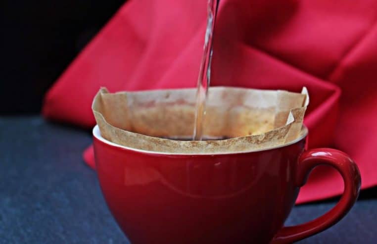 Eau versée dans un filtre posé sur une tasse rouge, illustrant la préparation manuelle d’un café filtre sur fond de tissu rouge.