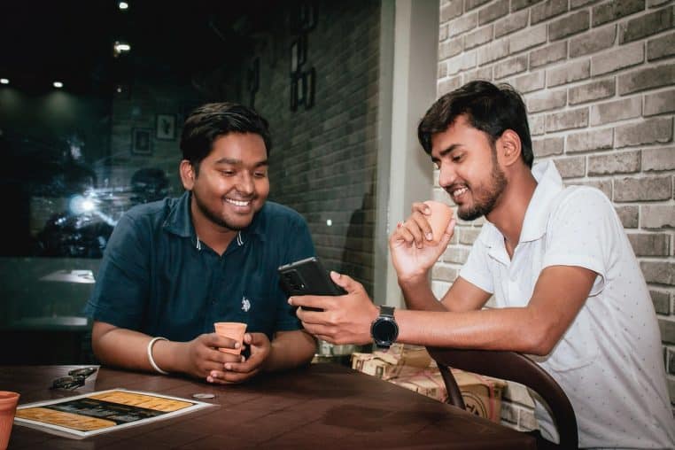 Deux personnes assises face à face dans un café, l’une parlant avec un léger sourire tandis que l’autre réagit avec une expression amusée.