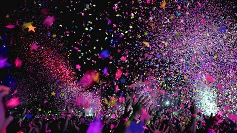 Scène de concert envahie de confettis colorés, foule compacte dans un club plongé dans une lumière violette.