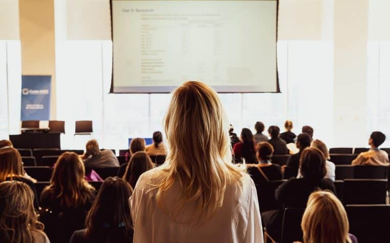 Orateur debout devant un auditoire en tenue professionnelle dans une salle de conférence, illustrant une formation d’entreprise en cours.