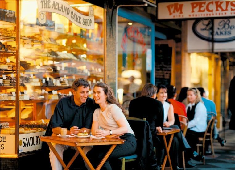 Couple assis à la terrasse d’un café, discutant autour d’un café et de verres d’eau, dans une ambiance urbaine et chaleureuse.