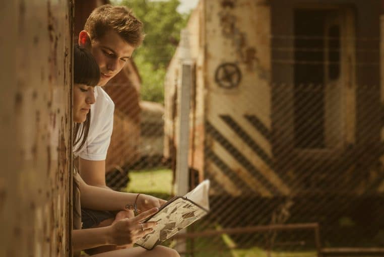Un couple assis côte à côte, concentré sur un même livre, dans un salon chaleureux à la lumière douce.