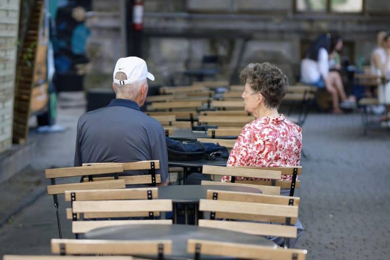 Couple installé en terrasse de restaurant, entouré de tables dressées, profitant ensemble d’un moment suspendu en plein air.