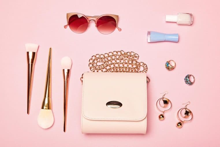 Accessoires de mode féminine disposés sur un fond rose, sac, bijoux et lunettes de soleil rappelant l’univers des enseignes de prêt-à-porter.