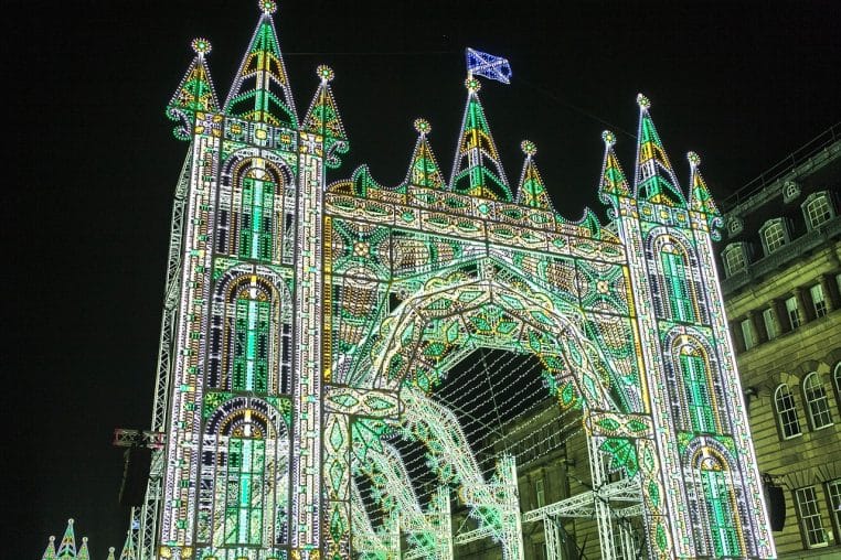 Château éclairé dominant les toits de la ville décorée pour Noël, avec les lumières du marché qui scintillent au premier plan.