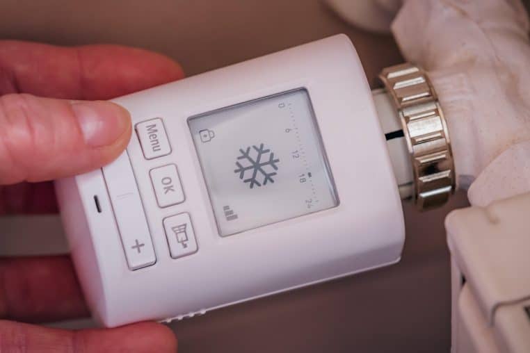 Main ajustant un thermostat mural numérique dans un couloir, pour gérer finement la température entre différentes pièces de la maison.