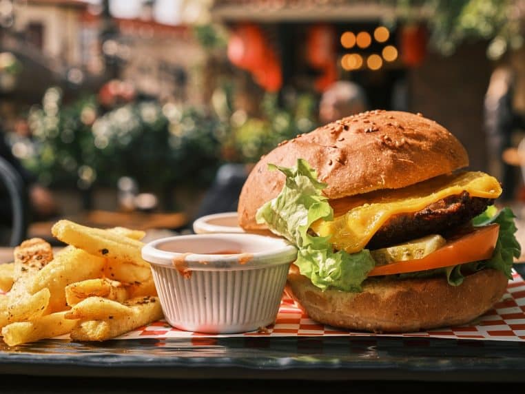 Hamburger garni, frites et boisson présentés sur un plateau de fast-food, avec emballages colorés en arrière-plan