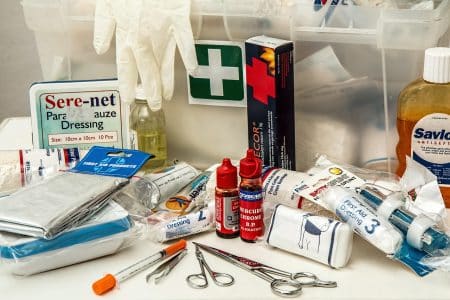 Trousse de premiers secours ouverte avec pansements, gants, flacons et compresses rangés dans un bac transparent, illustrant un kit d’urgence complet.