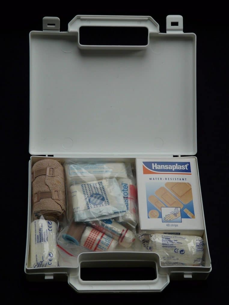 Boîte de premiers soins entièrement garnie de bandages, pansements et flacons, vue de dessus, montrant une organisation méthodique du matériel.