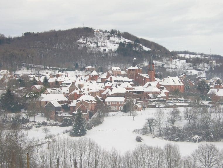 Village français niché au pied de collines enneigées avec toits, champs et arbres recouverts de neige après un épisode hivernal marqué
