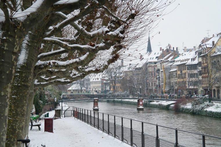 Paysage hivernal en France avec lac gelé, berges enneigées et rangée d’arbres nus se reflétant dans une eau immobile