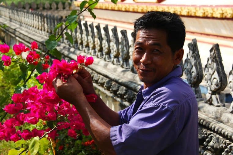 Jardinier au travail dans un grand jardin fleuri, vu de dos, entre massifs colorés et allées parfaitement entretenues.