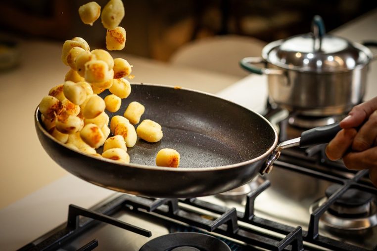 Gnocchis sautés en l’air dans une poêle au dessus d’un gazinière, en pleine cuisson, pour un effet croustillant et gourmand.