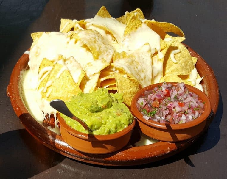 Bol de guacamole vert posé sur une table en bois, entouré de chips croustillantes prêtes pour un apéritif convivial.