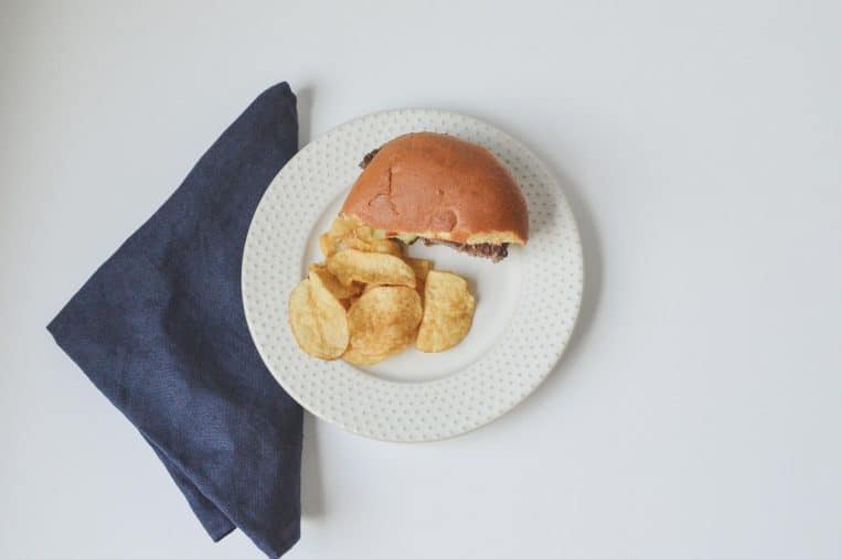 Gros plan sur un hamburger accompagné de frites sur une assiette blanche, servi dans un cadre de restauration rapide