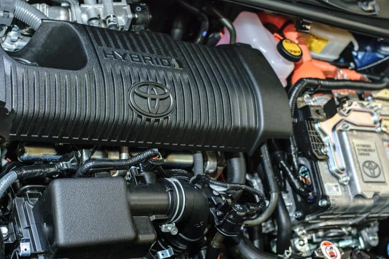 Gros plan sur le compartiment moteur d’une voiture hybride Toyota, montrant le bloc Hybrid Synergy Drive et les composants électriques associés.