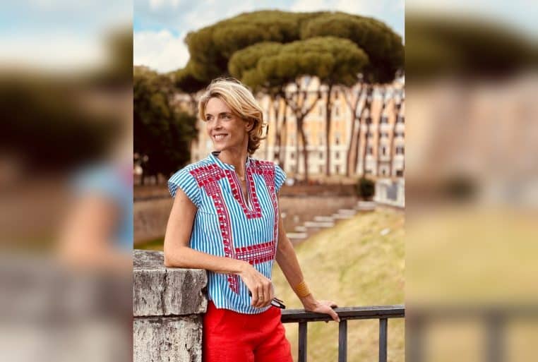 Julie Andrieu sourit appuyée à une rambarde à Rome, photographiée en extérieur, avec un fond urbain légèrement flouté.