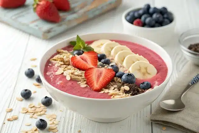 Gros plan sur un bol de kéfir rose garni de fruits frais et de céréales croustillantes sur une table blanchie.
