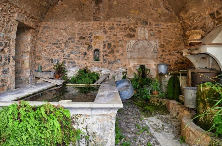 Ancien lavoir en pierre avec bassin et seaux en métal, évoquant le lavage du linge traditionnel avant les machines modernes et les parfums de lessive.