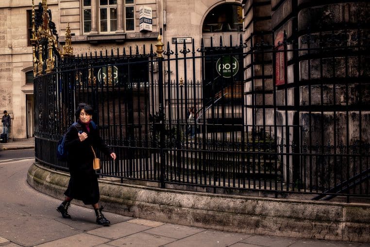 Femme marchant seule le long d’une rue londonienne bordée d’immeubles anciens, visiblement plongée dans ses pensées.