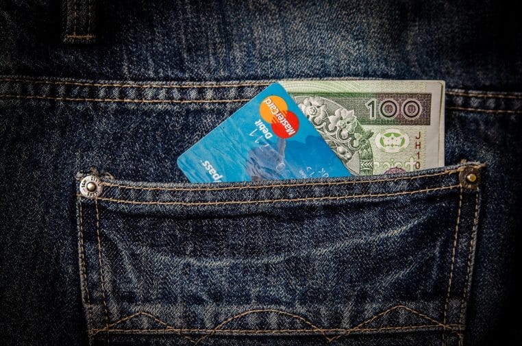 Billet et carte bancaire dépassant d’une poche de jean, illustrant la coexistence entre espèces et paiement par carte au quotidien.